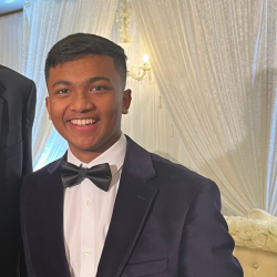 a young man in a black suit smiles at the camera