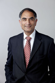 Professor Raj Thakker sytands hands in pockets, wearing a blue suit, a red and white striped tie and a white shirt